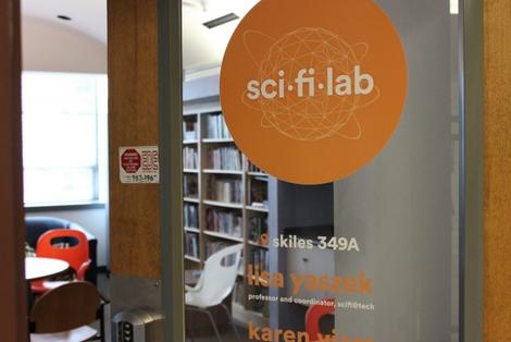 Exterior photo of the Sci Fi Lab door showing the lab's logo and bookcase behind it.